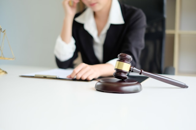 A girl wearing a suit sitting at a table with a gavel next to her.